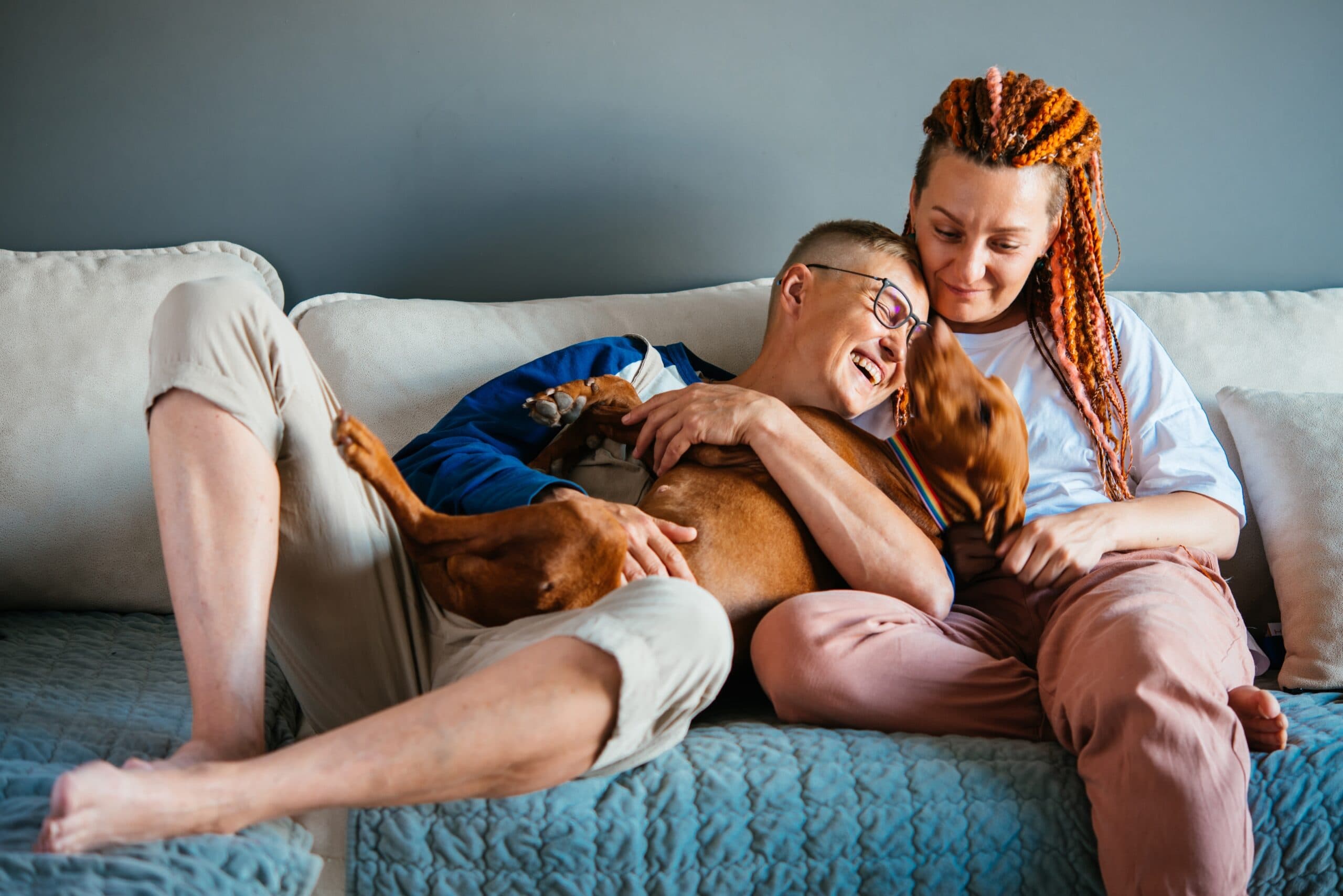 Beautiful,Lesbian,Couple,Cuddling,With,Their,Dog,On,The,Couch.